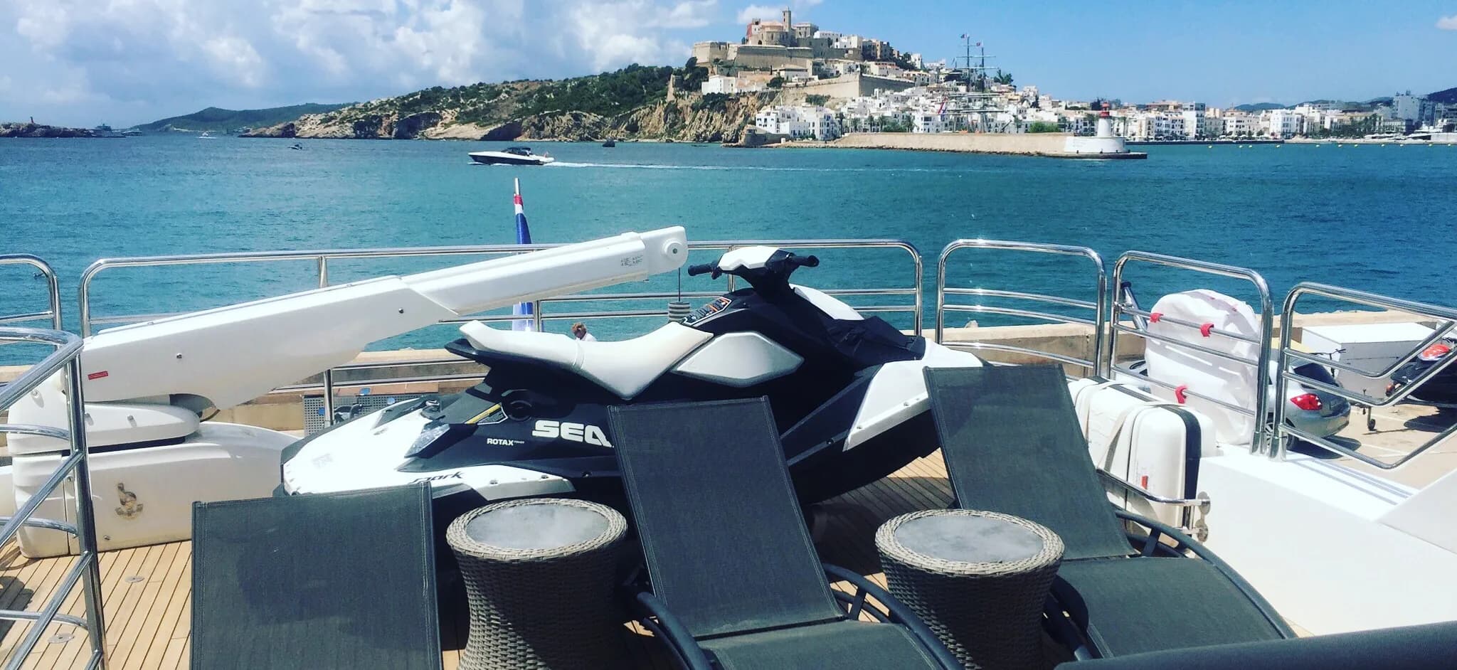 Sun loungers and a jet ski on the deck of a yacht, with Dalt Vila and Ibiza Town across the water